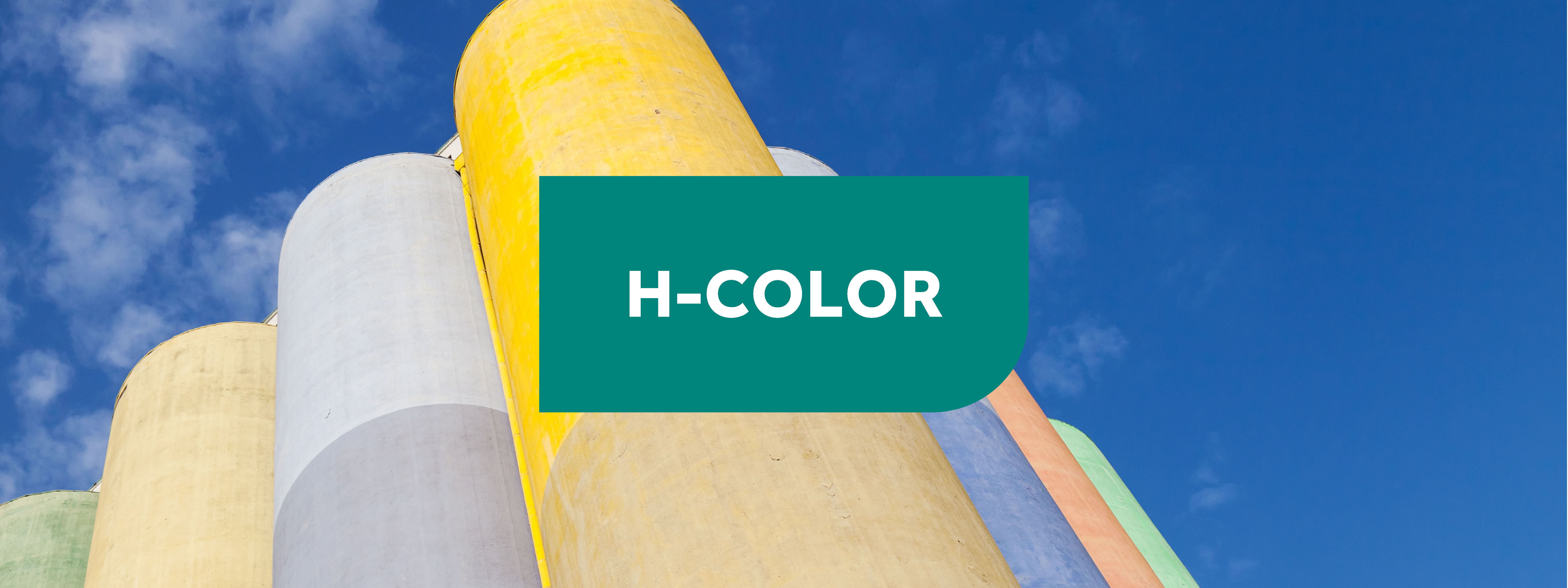 Imagen picada de un silo detrás del que hay tres más a la derecha y tres más a la izquierda formando un triángulo de cilindros en colores pastel, con un fondo de cielo azul. Sobre la imagen, un cartel en el centro de color verde con las letras en blanco "H-COLOR".