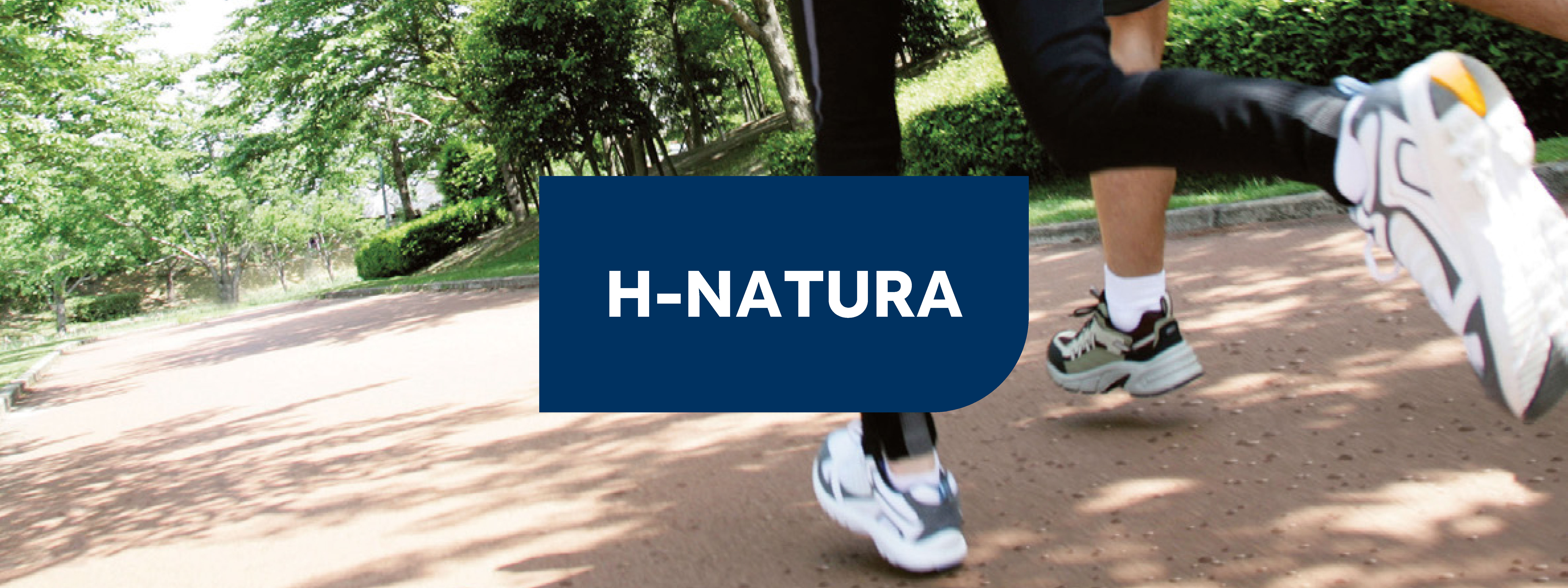 camino de tierra prensada natural marron claro y se ven las piernas de dos corredores a la derecha que hacen footing uno con mallas y zapatillas blancas y el otro con pantalones cortos, calcetines blancos y zapatillas azul claro. 
