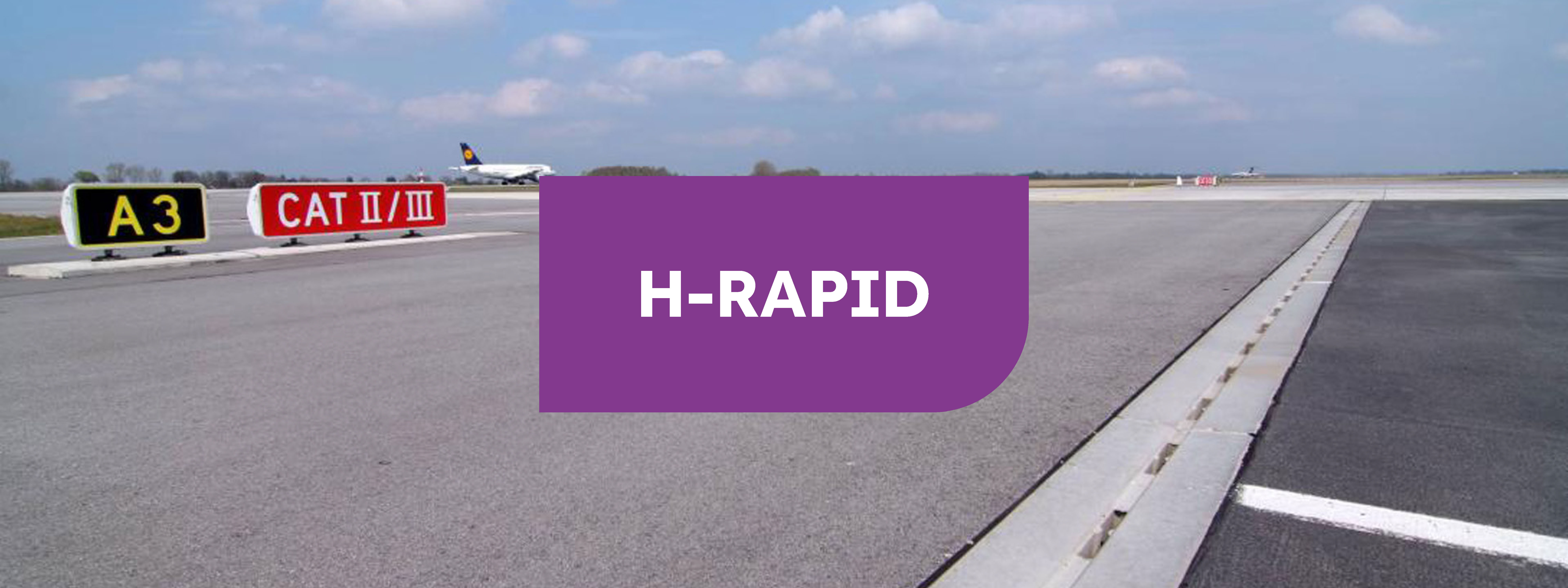 Pista de asfalto en un aeropuerto con señalización para aviones y cartel en el centro en marron con las letras "H-RAPID" en blanco.