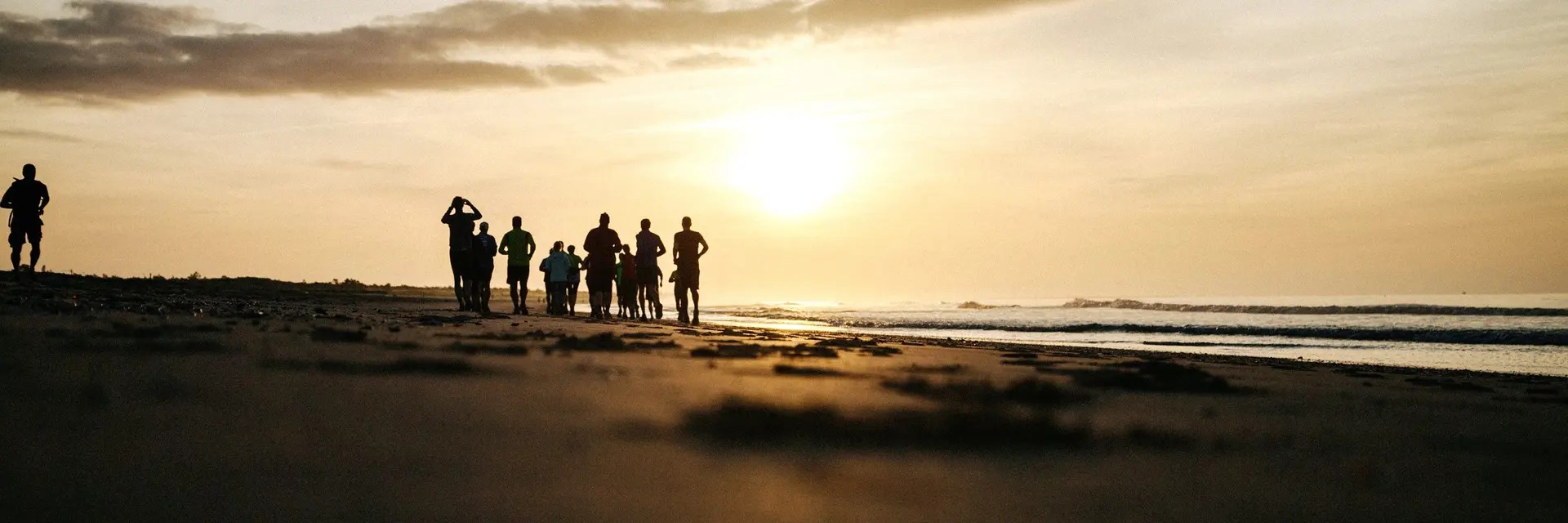 Un grupo de personas pasean por la playa con el sol a contraluz.