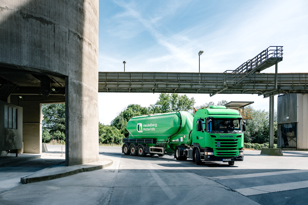Camión de mezcla verde de Heidelberg Materials estacionado en un sitio industrial bajo un puente elevado.