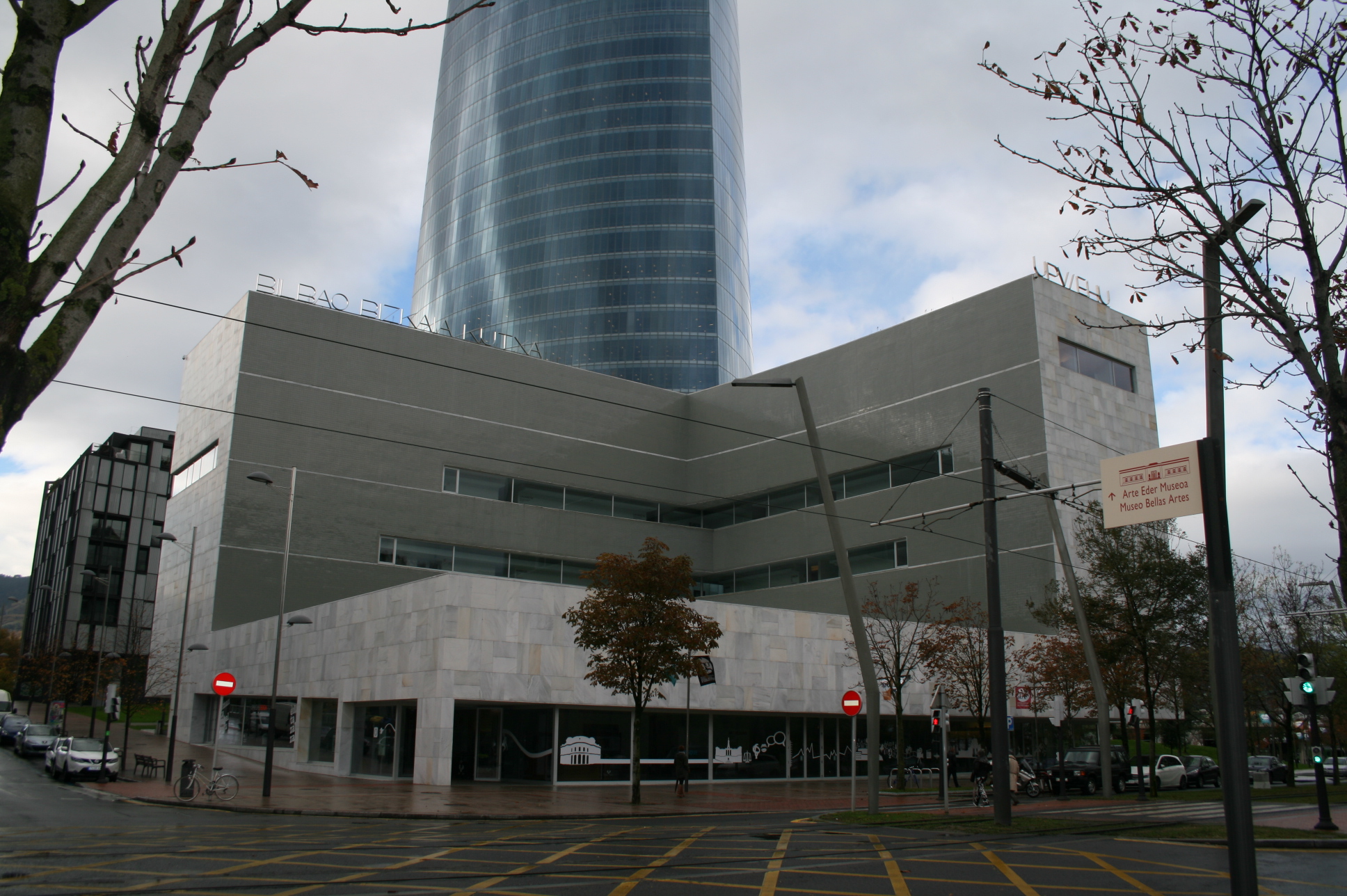 Edificio en forma de L con torre detrás.