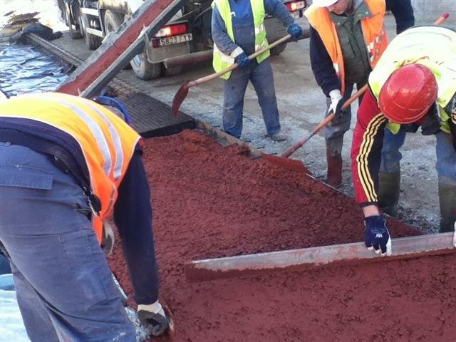 Cuatro operatios reparten el hormigón coloreado en la construcción de un camino.