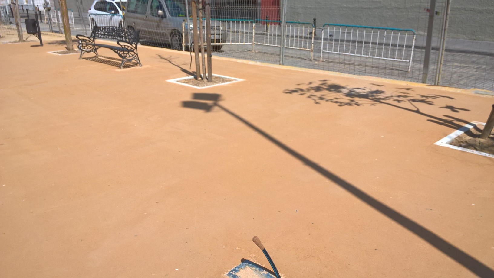 Detalle de suelo de arena compactada color marrón en parque junto a árboles jóvenes y vallas metálicas