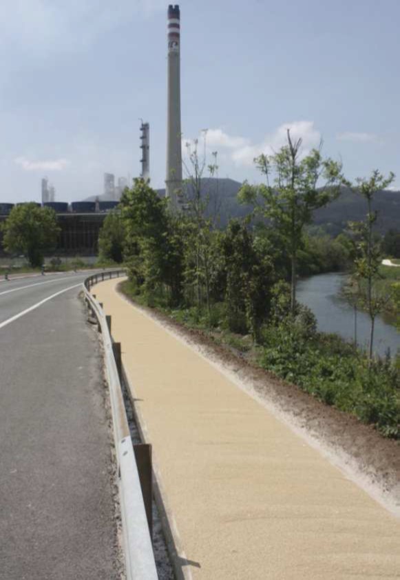 Camino de tierra rodeado de árboles a la derecha y carretera a la izquierda