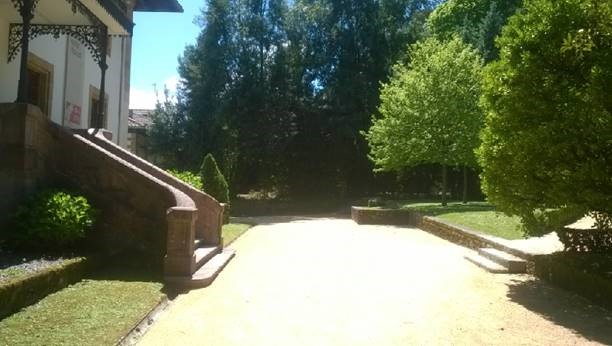 Sendero de parque con árboles a la derecha, cesped y la entrada de un edificio clásico a la izquierda.