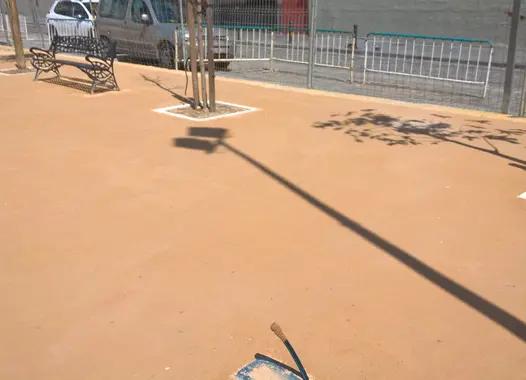 Detalle de suelo de arena compactada color marrón en parque junto a árboles jóvenes y vallas metálicas